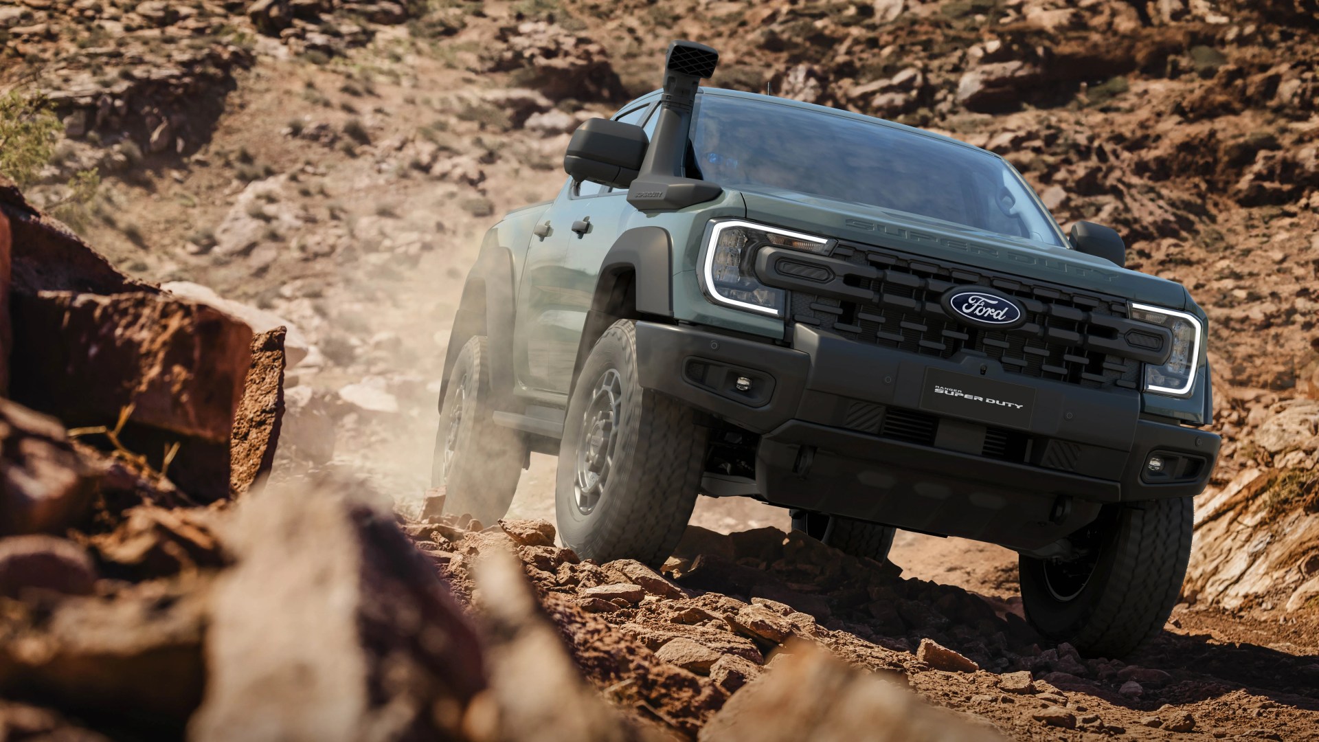 Green Ford Super Duty pickup truck with snorkel driving on rocky off-road terrain.