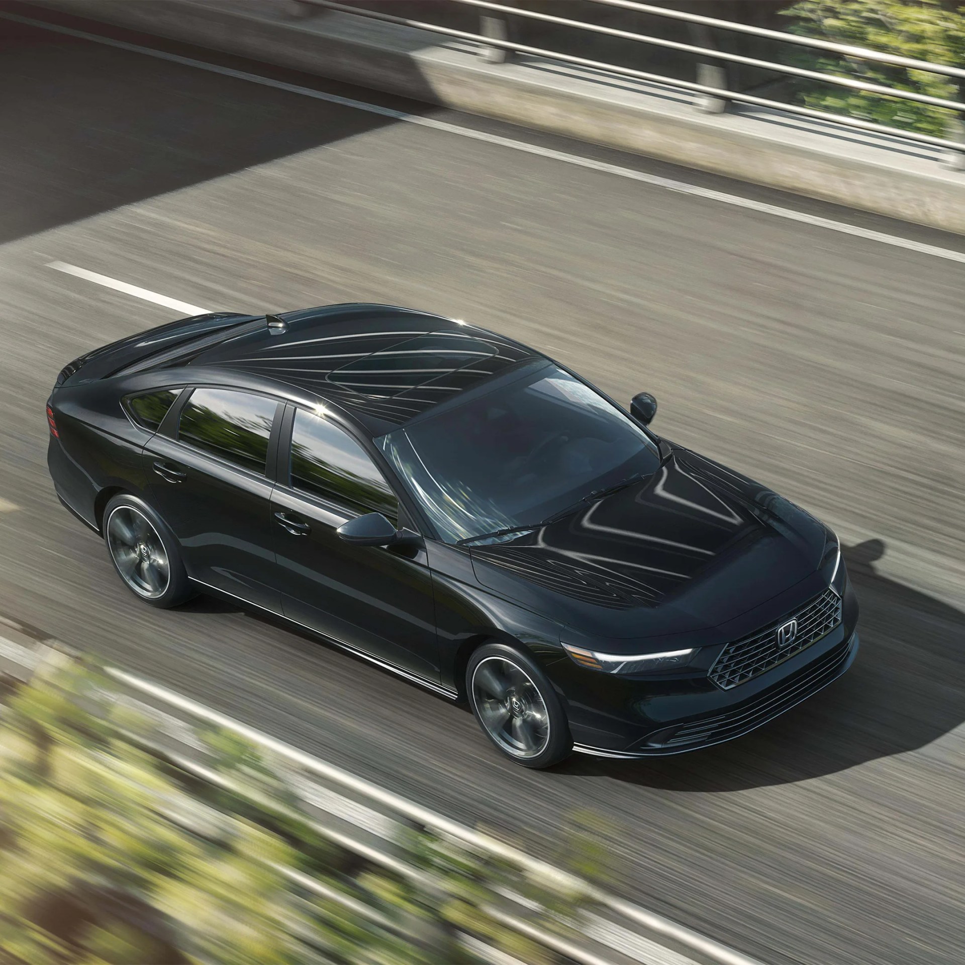 Black Honda sedan with sleek design driving on a highway with reflections on the roof and windows.