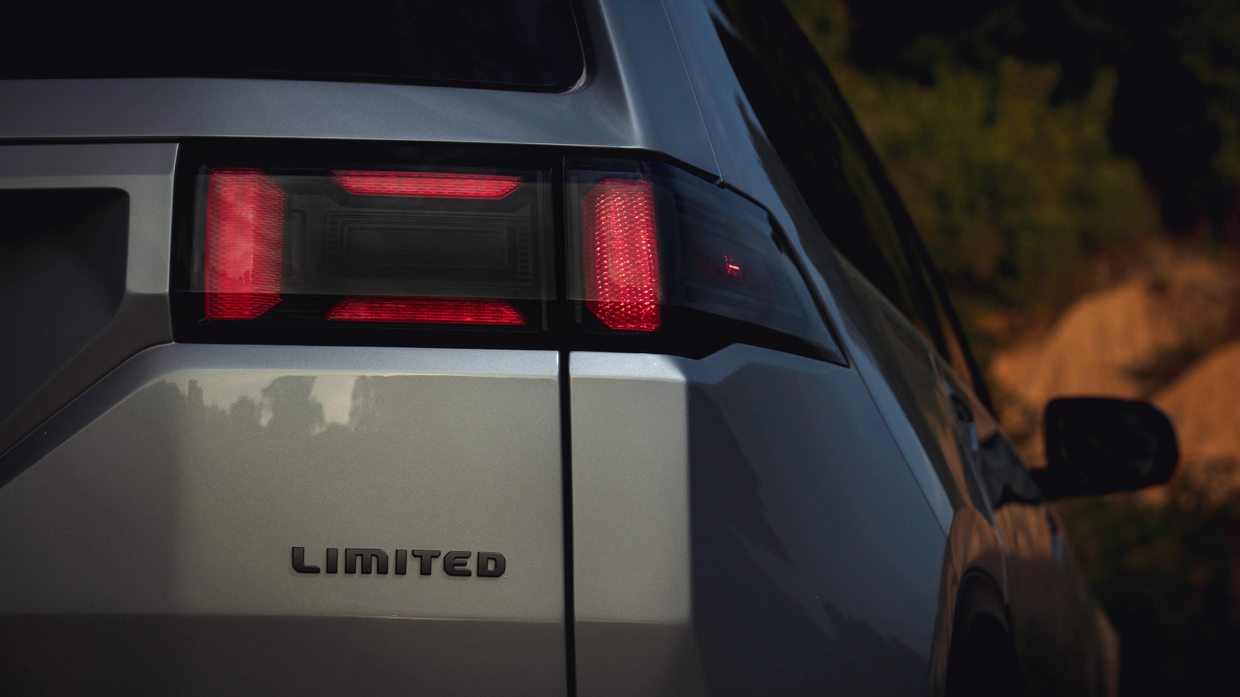 Silver car rear with illuminated red taillight and "LIMITED" badge on the trunk.
