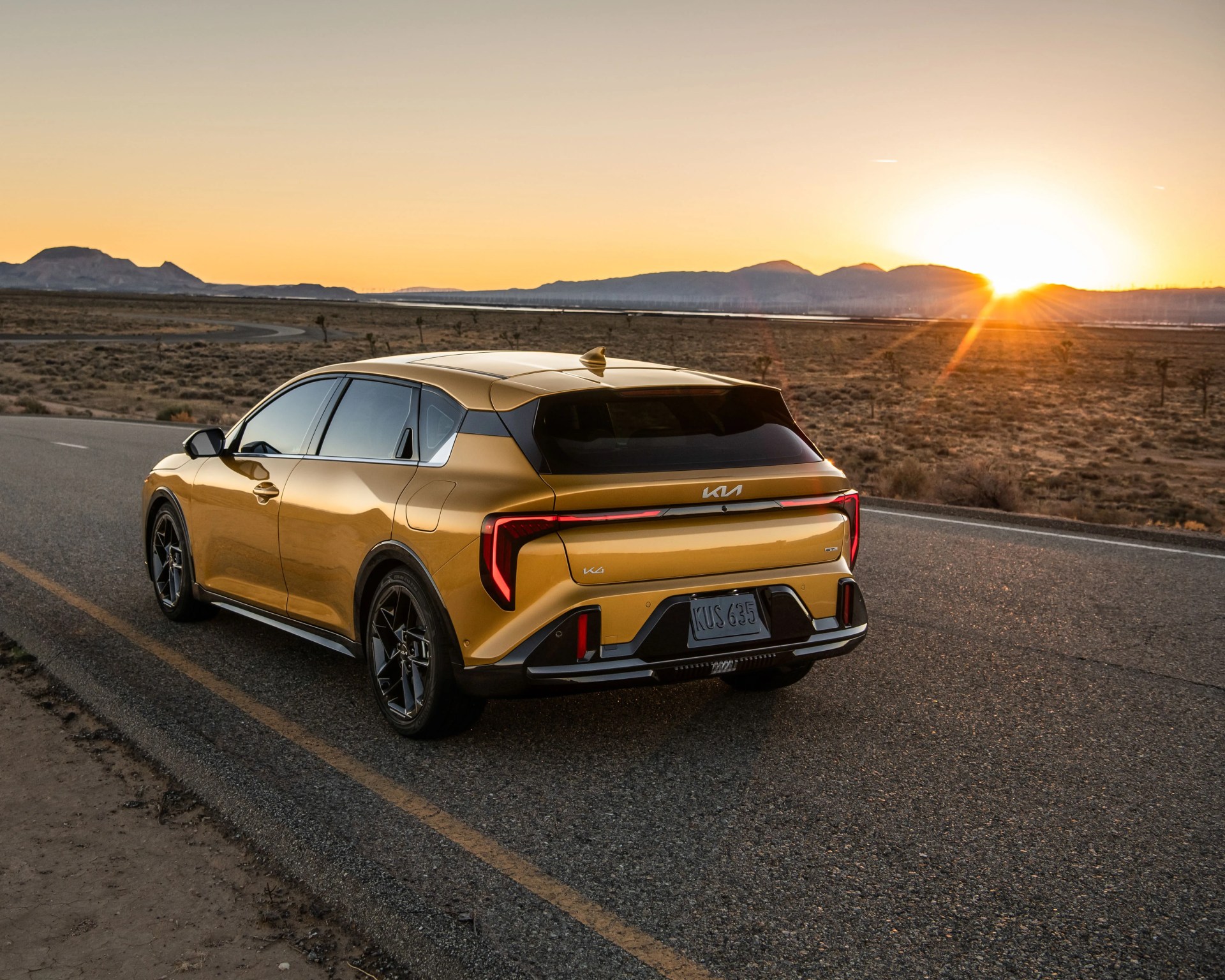 Gold Kia EV6 electric SUV parked on a desert road at sunset with mountains in the background.