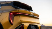 Rear view of a gold Kia K4 with illuminated taillights at sunset.