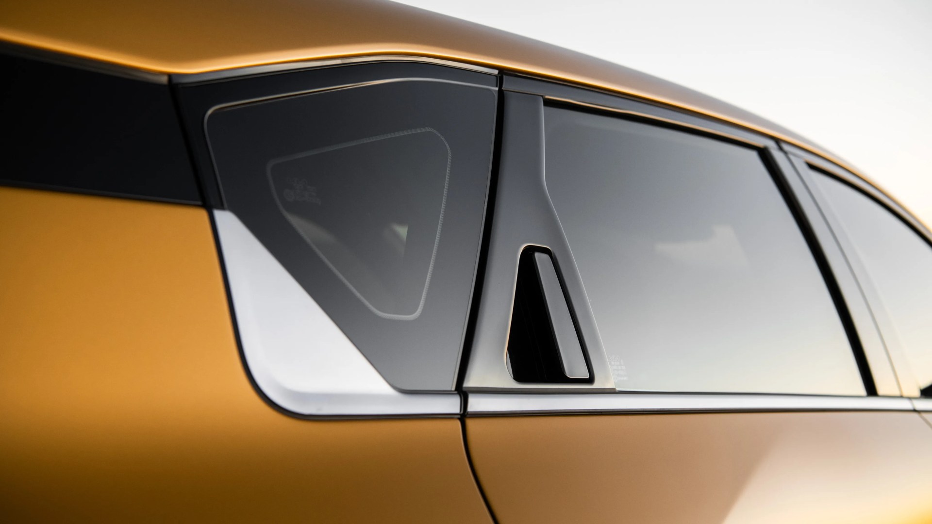 Close-up of a gold car's rear side window with black trim and a small triangular vent window.