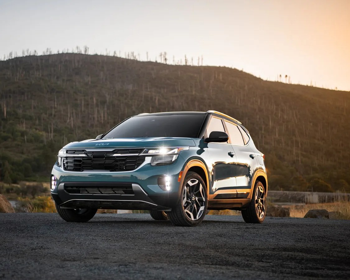 Blue Kia SUV with black grille and alloy wheels parked on a gravel road at sunset.