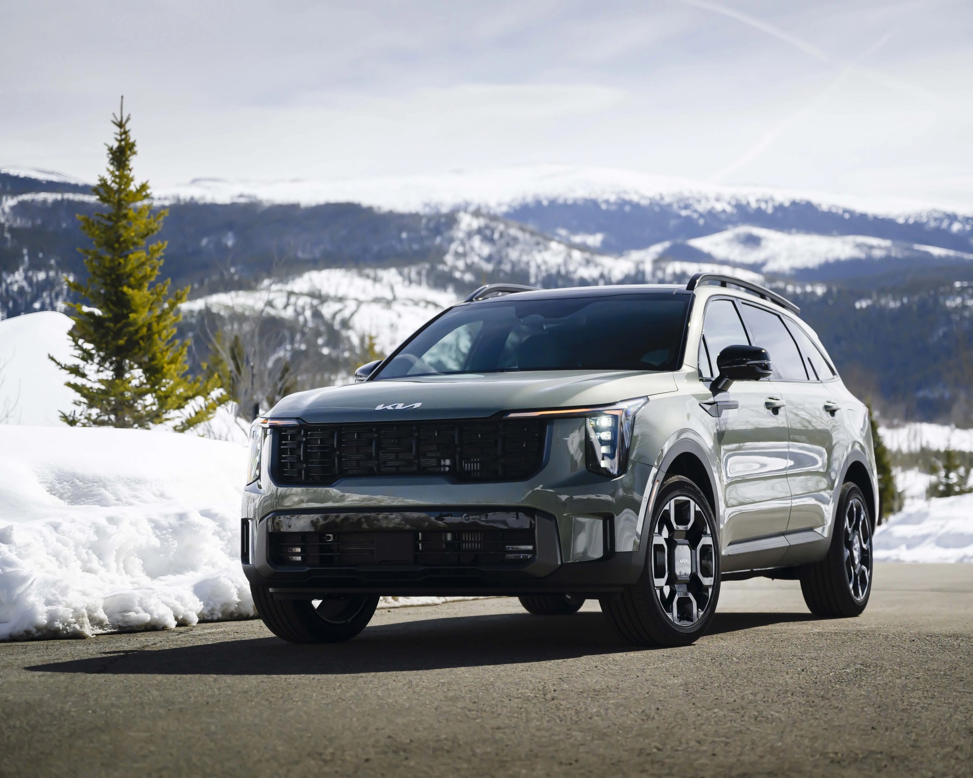 Gray Kia SUV parked on a snowy mountain road with snow-covered hills in the background.