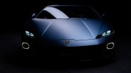Front view of a blue Lamborghini sports car with illuminated headlights and hexagonal daytime running lights in a dark setting.