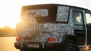 Rear side of a black SUV with white and black abstract camouflage wrap and a spare tire cover, parked at sunset.