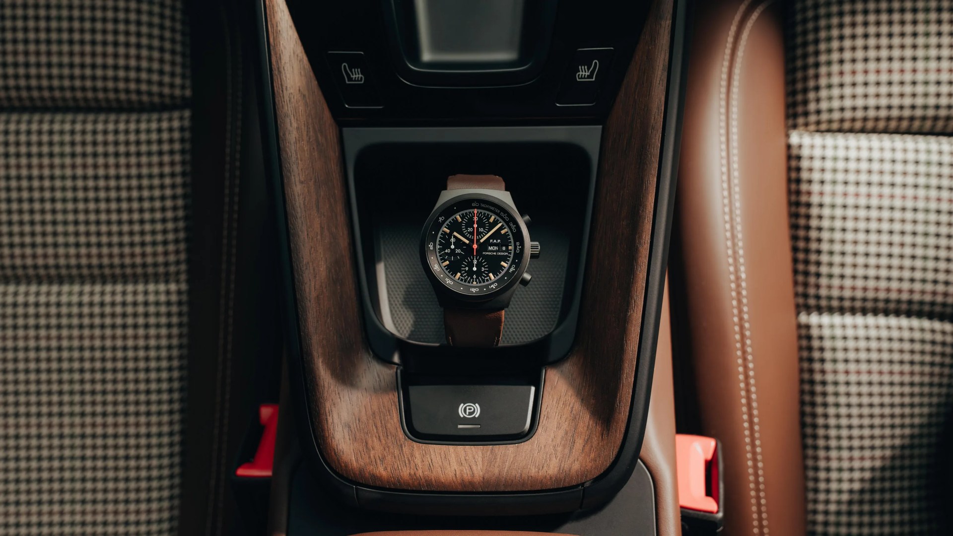 Black chronograph wristwatch with brown leather strap placed in a car's wooden center console compartment.