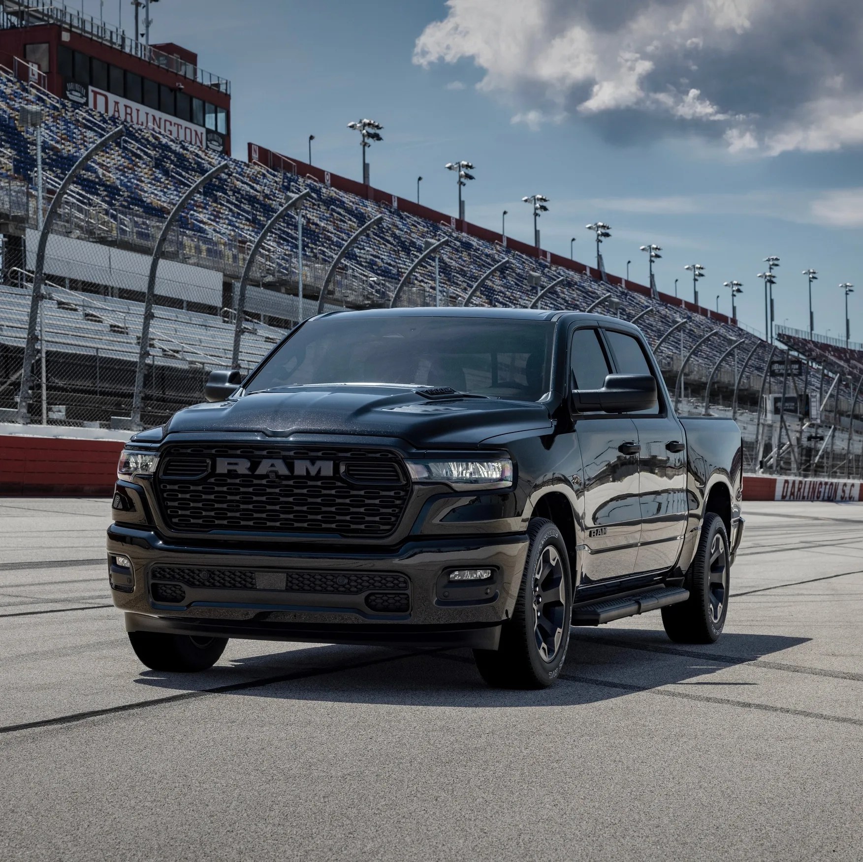Black RAM pickup truck parked on a racetrack with empty grandstands in the background.