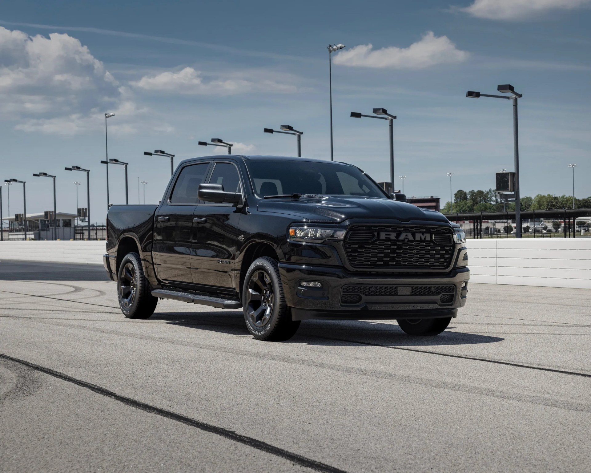 Black RAM pickup truck parked on a racetrack under a partly cloudy sky.