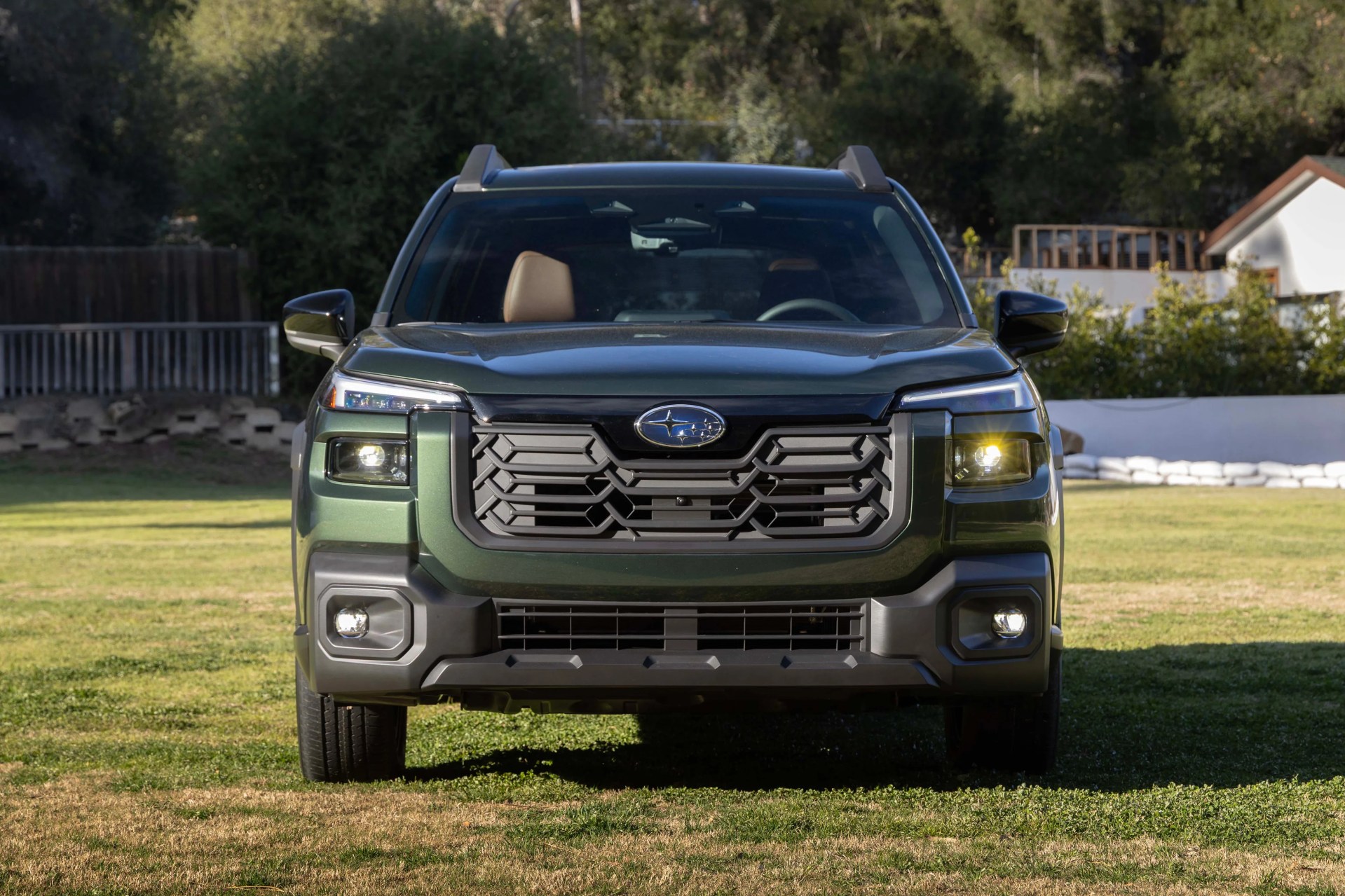 Front view of a dark green Subaru SUV with LED headlights on a grassy lawn.