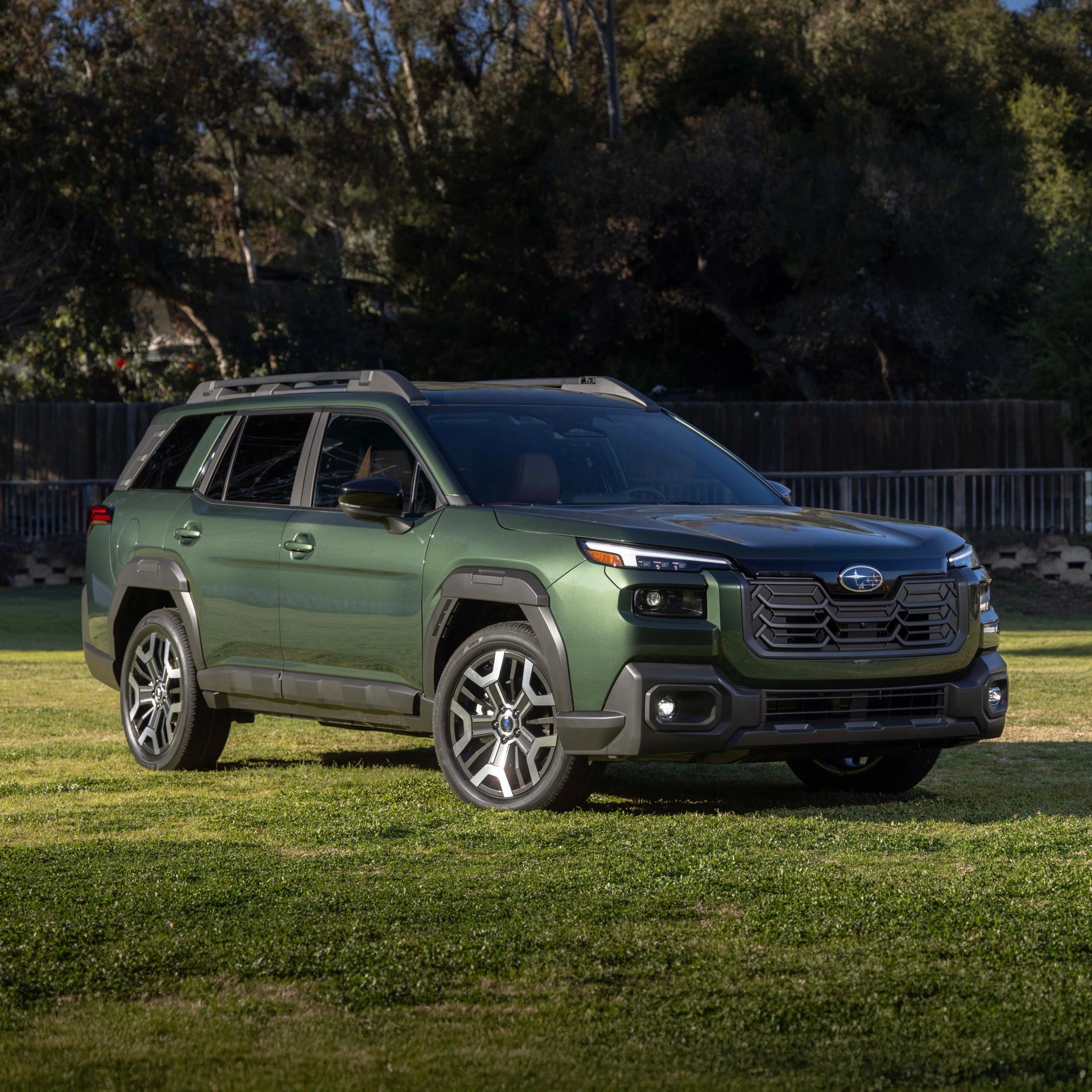 Green Subaru SUV with black grille and roof rails parked on grass with trees in the background.