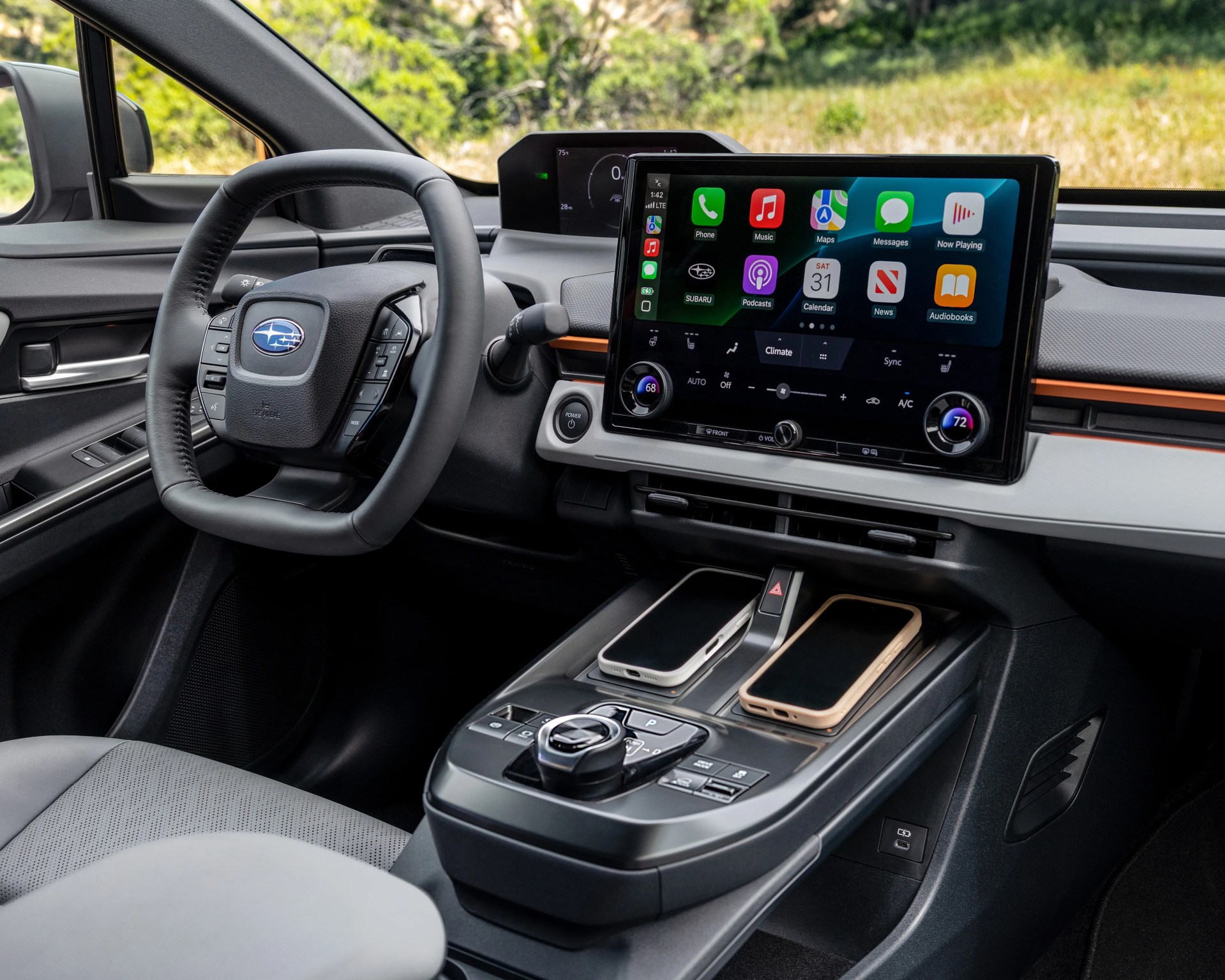 Car interior showing a Subaru steering wheel, large touchscreen display with apps, and two smartphones on the center console.