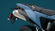 Rear section of a blue Suzuki motorcycle showing the exhaust, seat, and rear tire against a teal background.