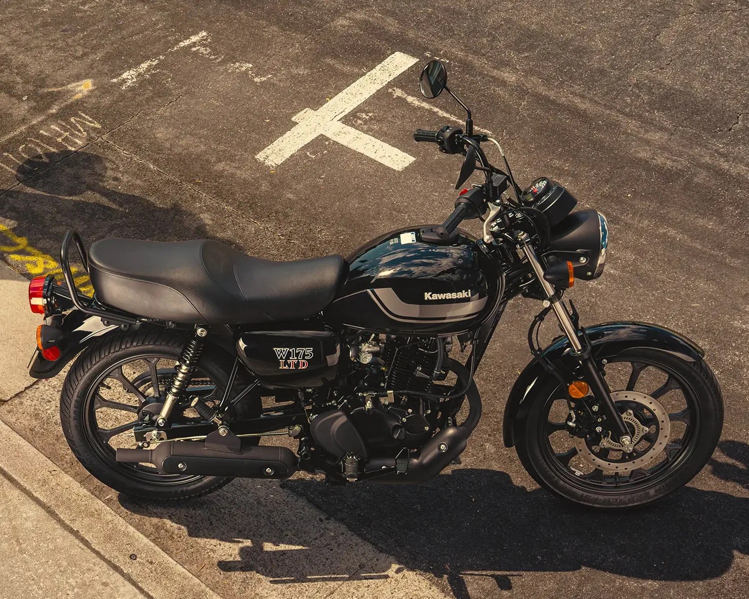 Black Kawasaki W175 LTD motorcycle parked on asphalt near a concrete curb.