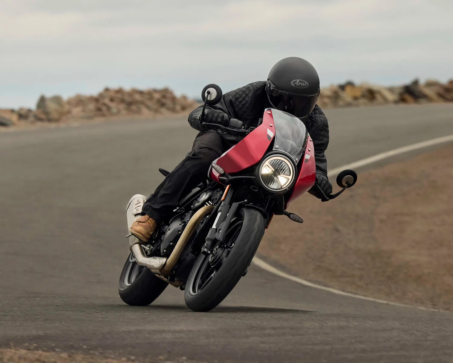 Motorcyclist wearing black gear and helmet riding a red and black motorcycle leaning into a turn on a paved road.