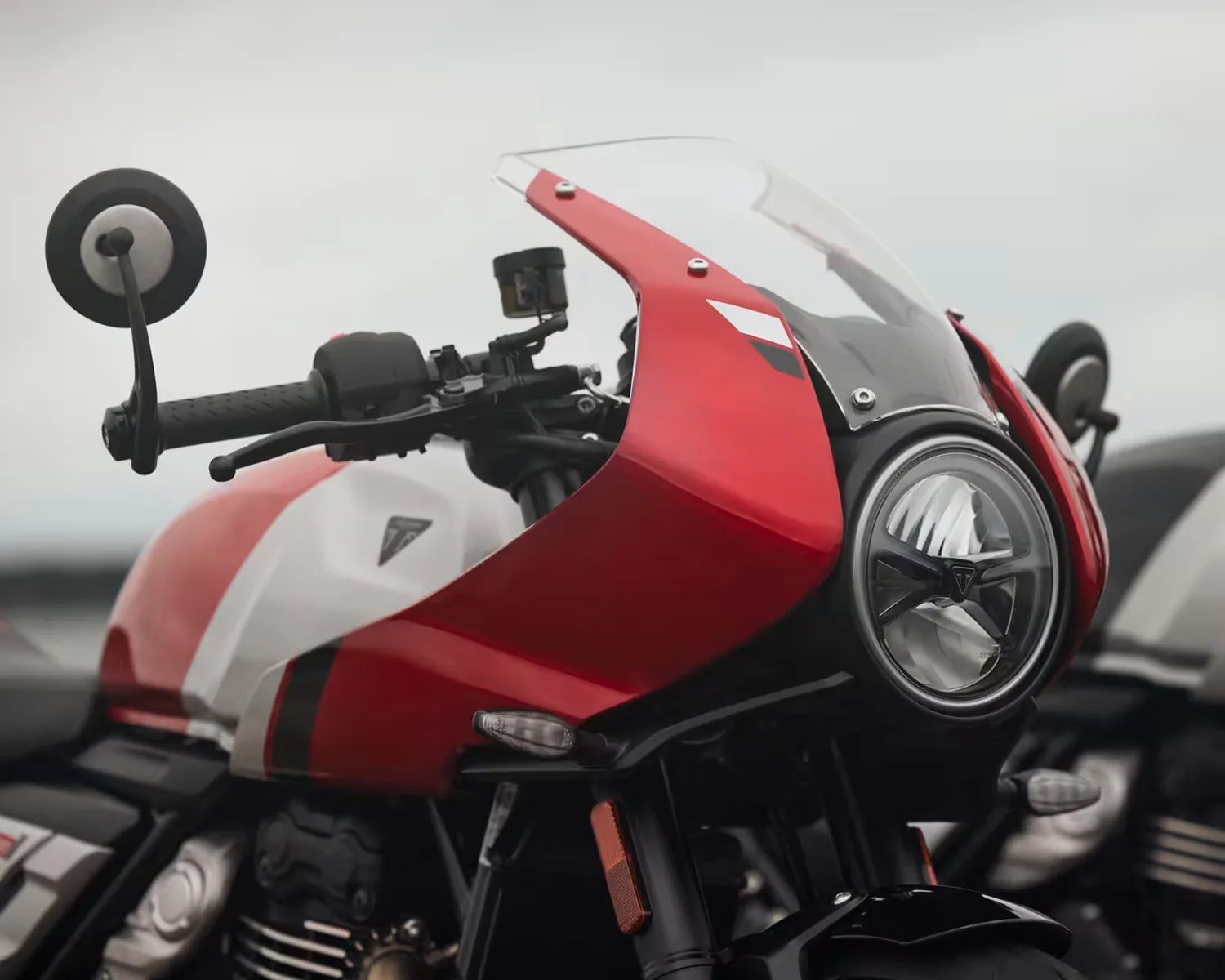 Red and white motorcycle front with round headlight and clear windshield.