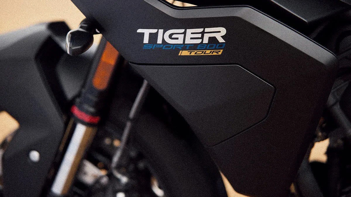 Close-up of a black motorcycle panel with "TIGER SPORT 900 TOUR" decal in white, blue, and yellow.