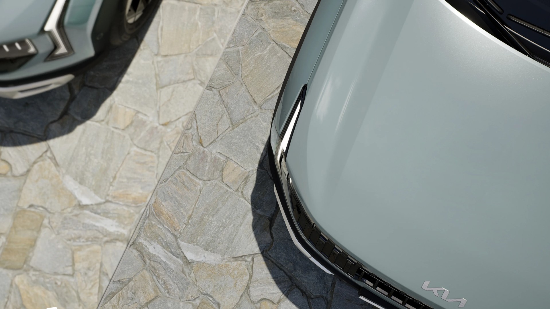 Close-up of the front hood and grille of a light gray Kia car parked on a stone pavement.