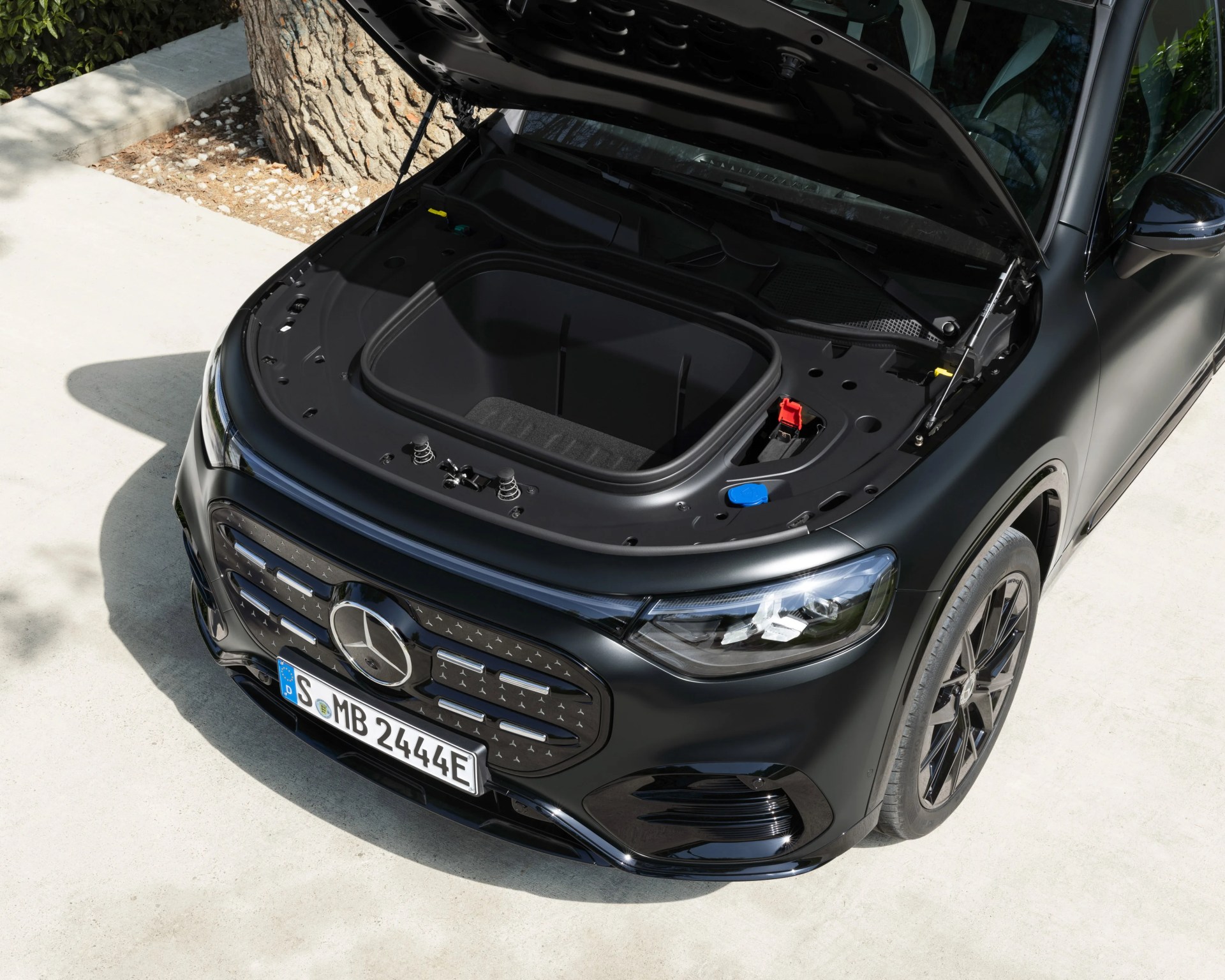 Black Mercedes-Benz electric car with open front trunk parked on a concrete surface.