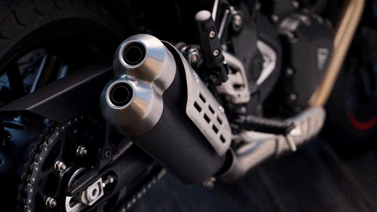 Close-up of a motorcycle's dual exhaust pipes with a black and silver finish near the rear wheel and chain.