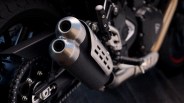 Close-up of a motorcycle's dual exhaust pipes with a black and silver finish near the rear wheel and chain.