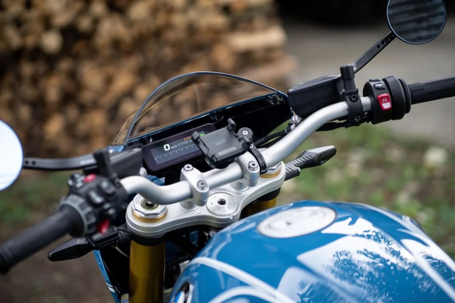 Blue motorcycle fuel tank with white graphics and digital speedometer on handlebars.