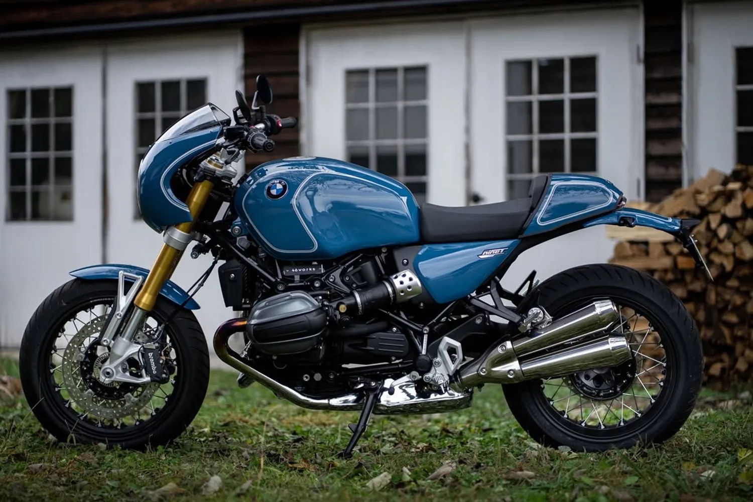 Blue BMW motorcycle with gold front forks and dual chrome exhausts parked on grass.