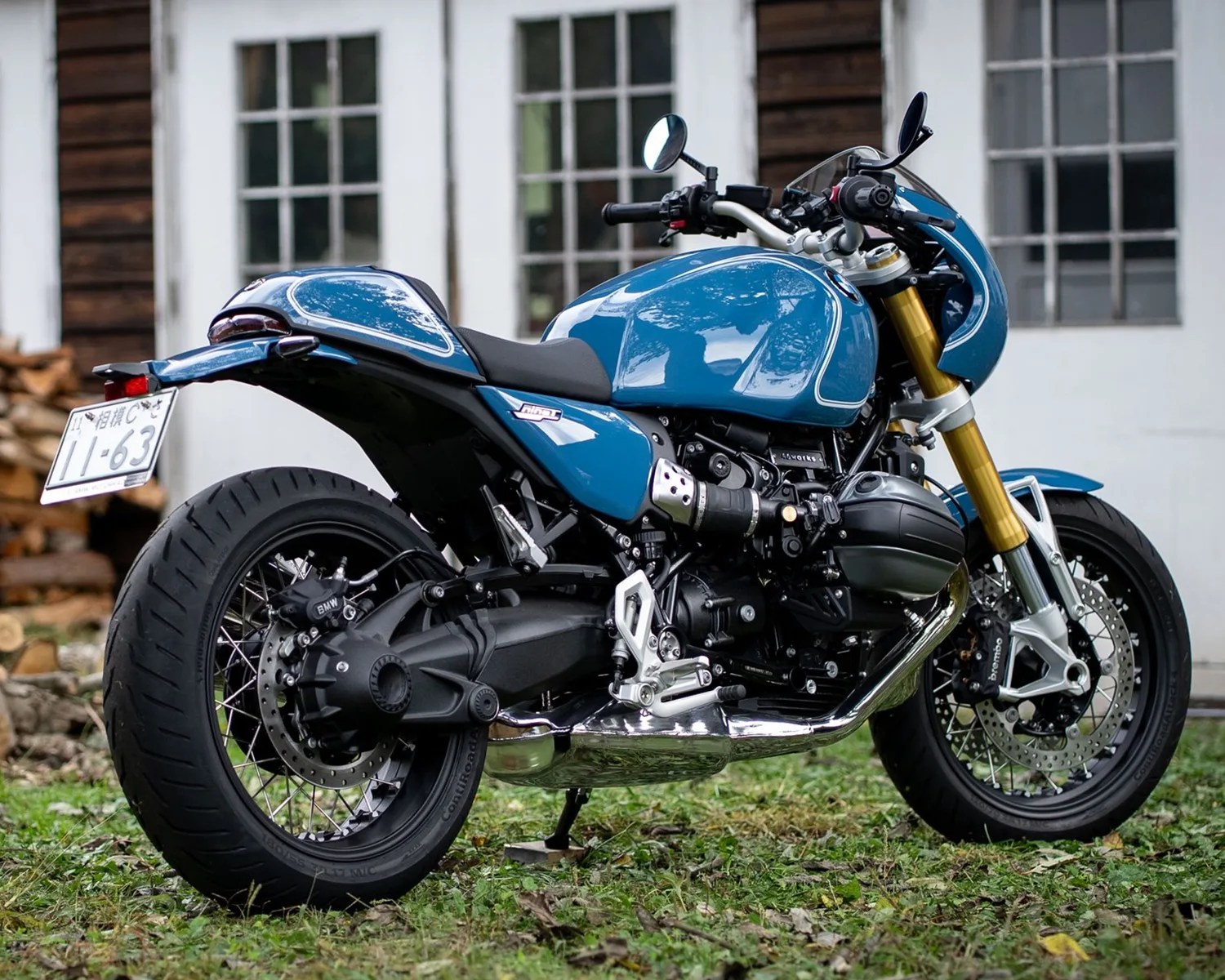 Blue BMW motorcycle with gold front forks and black tires parked on grass in front of a building.
