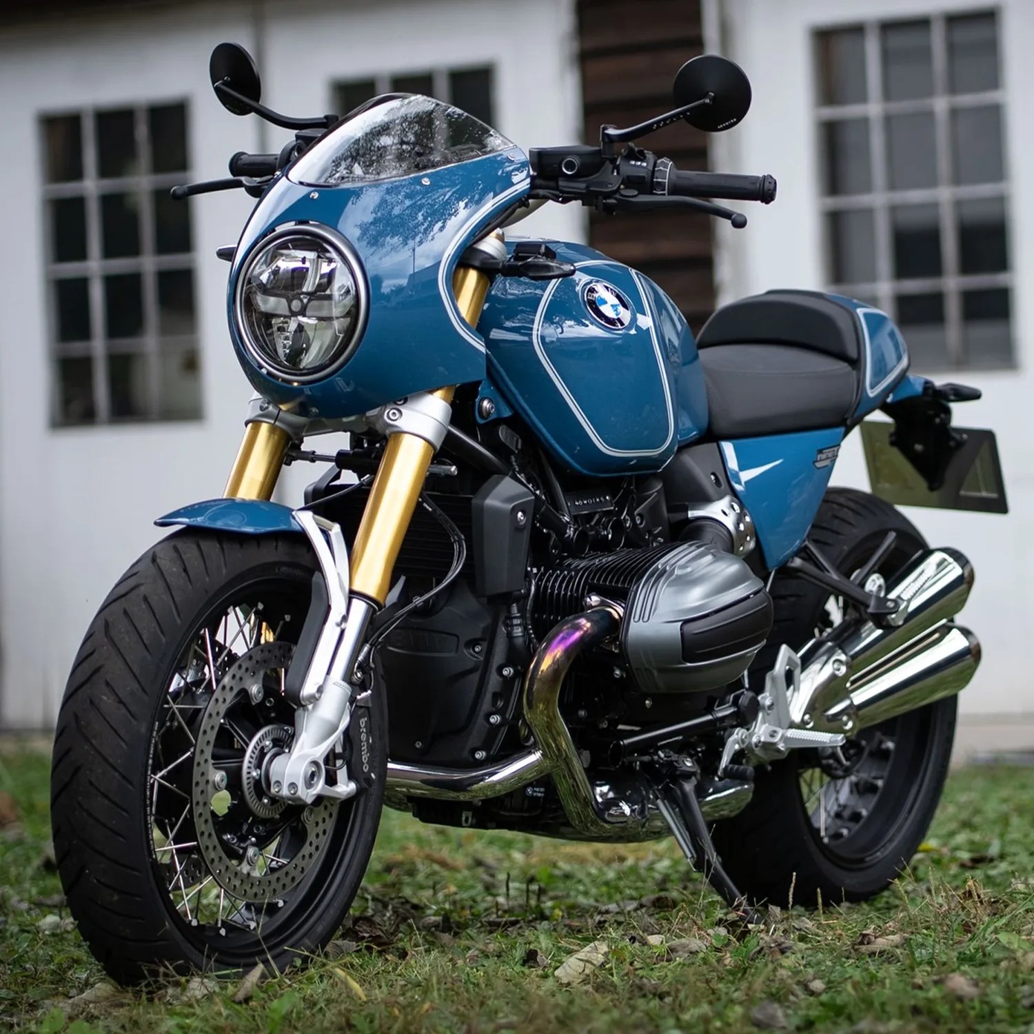 Blue BMW motorcycle with gold front forks and round headlight parked on grass.
