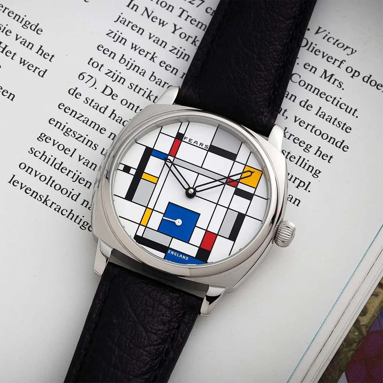 Silver wristwatch with a black leather strap and a geometric dial featuring red, blue, yellow, and black lines and squares.