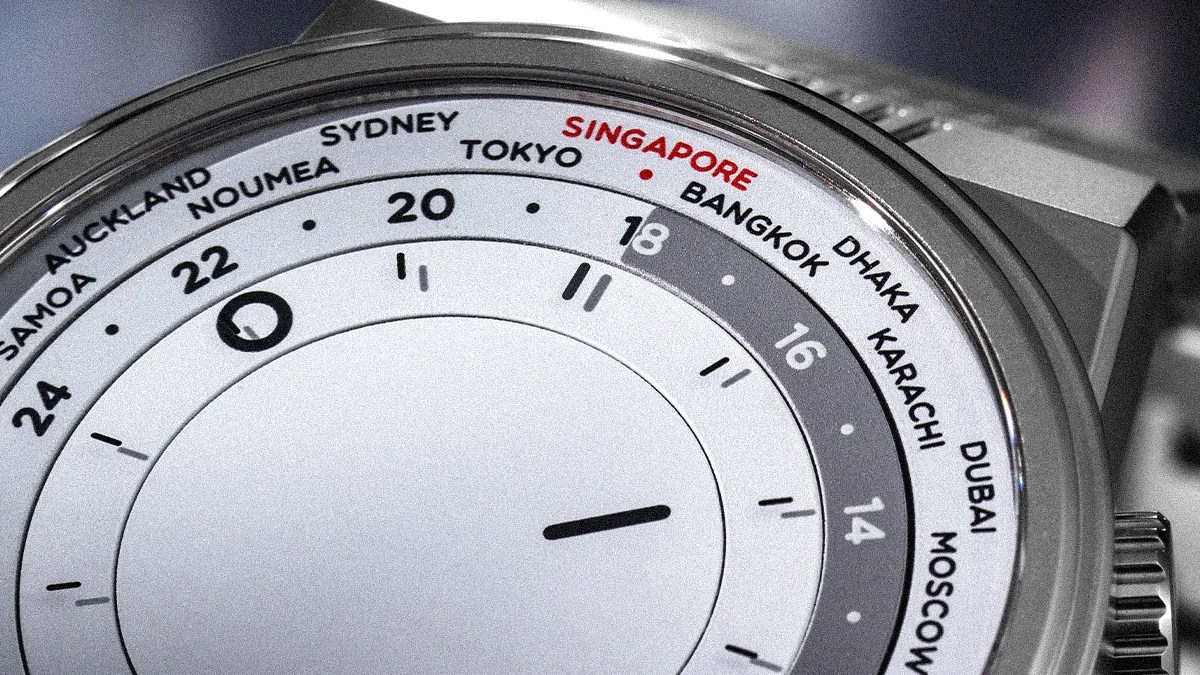 Close-up of a silver world time watch showing cities including Singapore, Tokyo, and Sydney on the bezel.