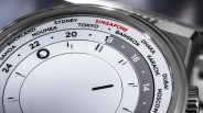 Close-up of a silver world time watch showing cities including Singapore, Tokyo, and Sydney on the bezel.