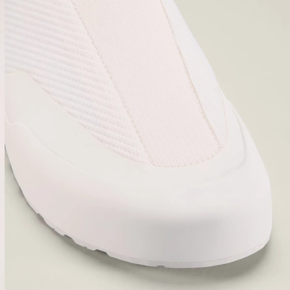 Close-up of the toe area of a white sneaker with textured fabric and a smooth rubber sole.