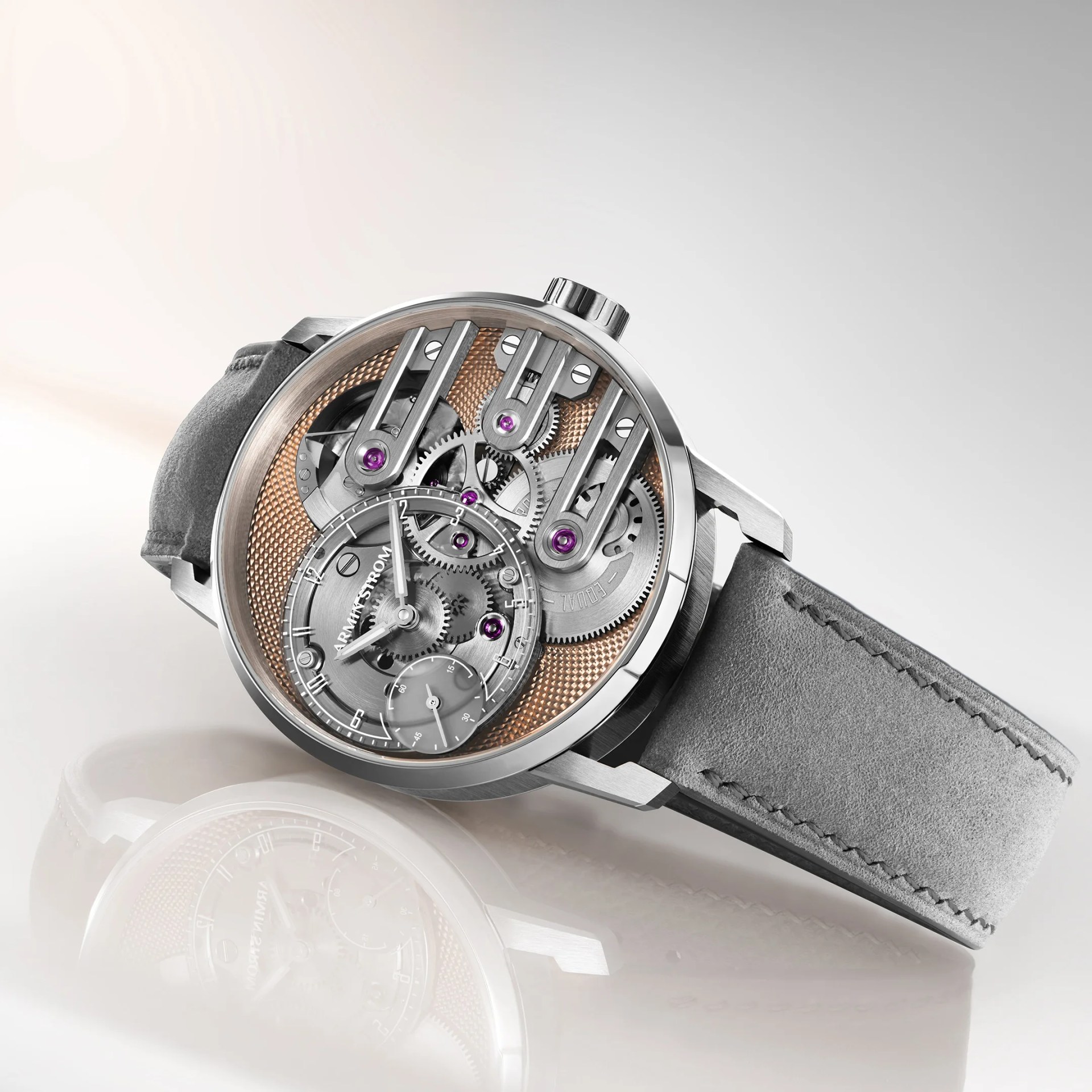 Silver mechanical wristwatch with visible gears and purple jewels, featuring a textured copper background and gray suede strap.