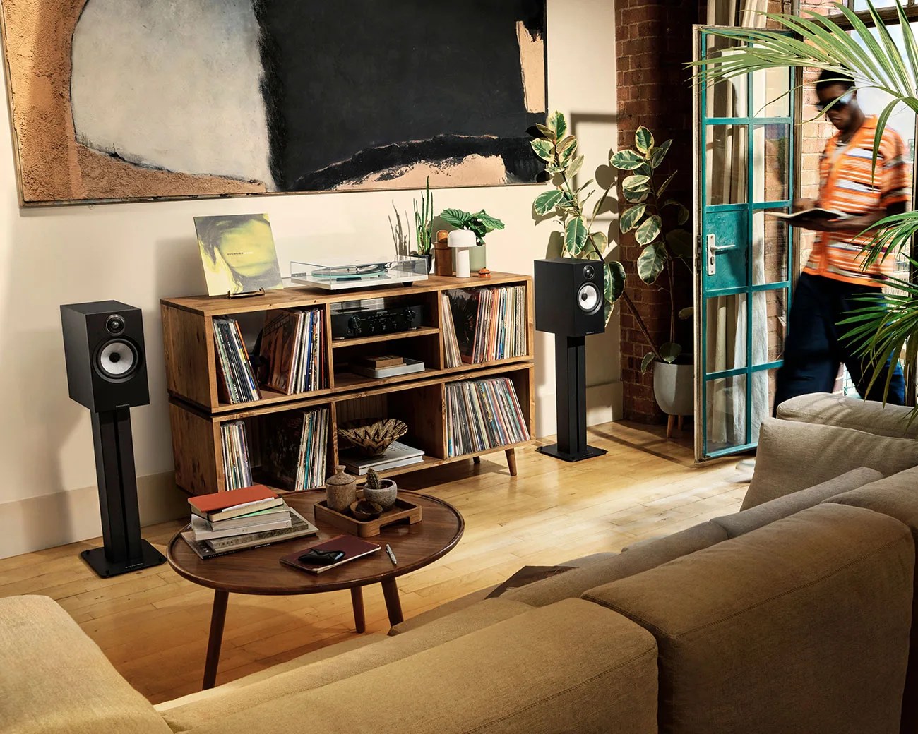 Living room with beige sofa, wooden coffee table with books, wooden record shelf with vinyls and speakers on stands.