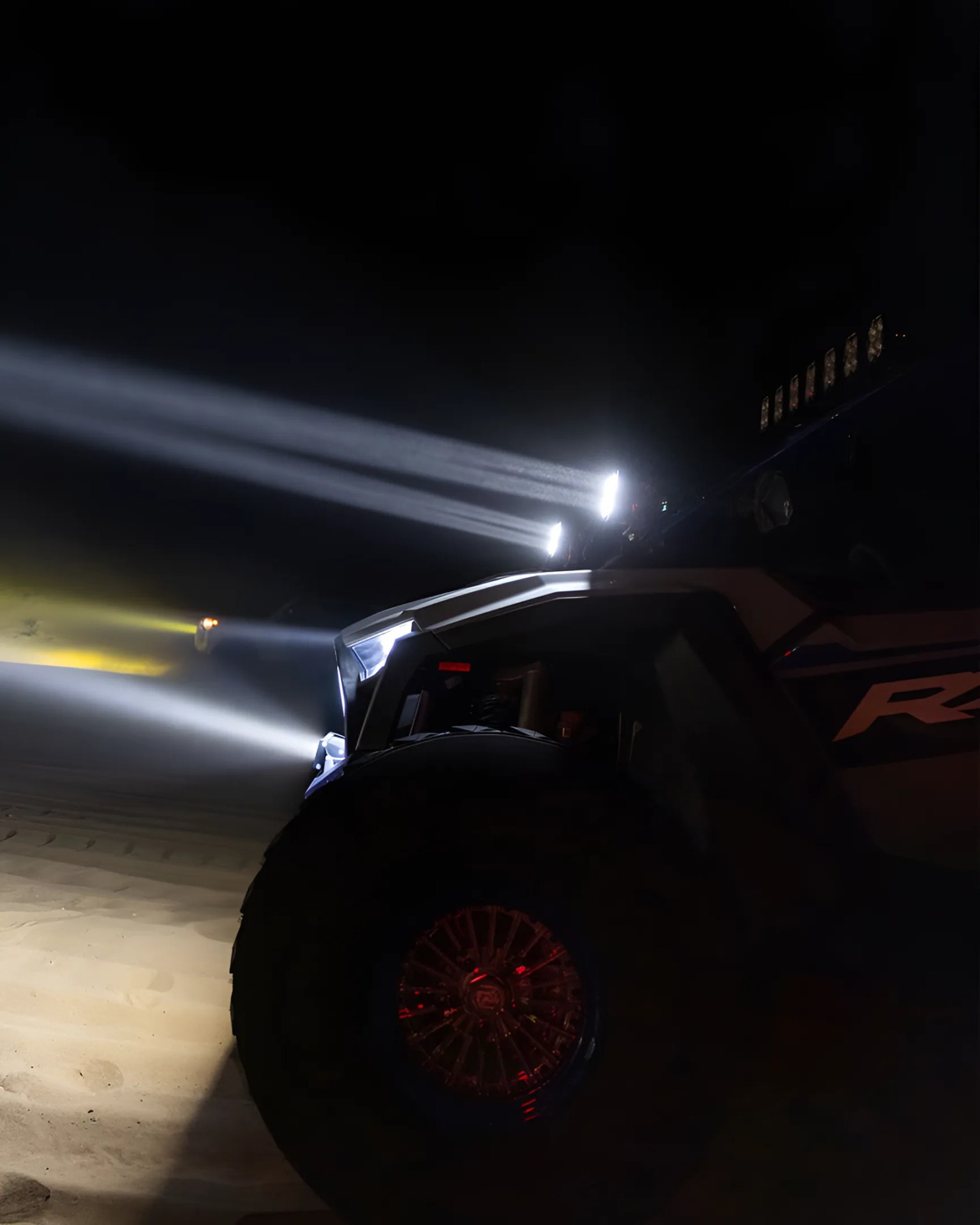 Off-road vehicle with bright LED lights on roof and front shining into dark night.