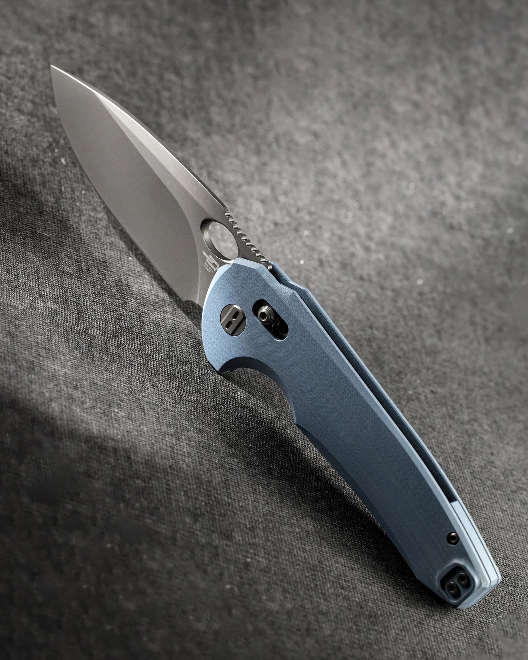Folding knife with a matte silver blade and textured light blue handle on a gray fabric surface.