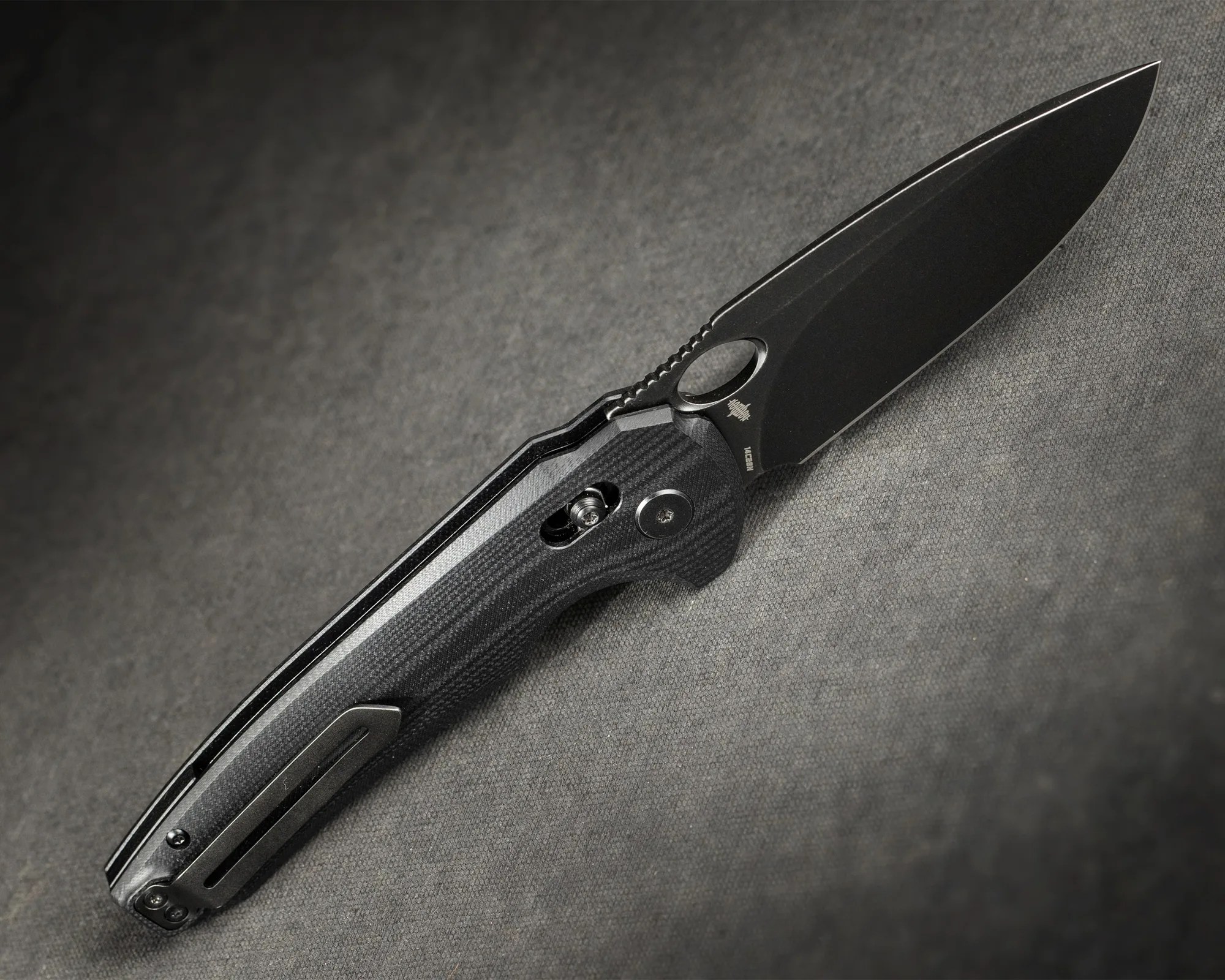 Black folding knife with textured handle and clip on a gray fabric surface.