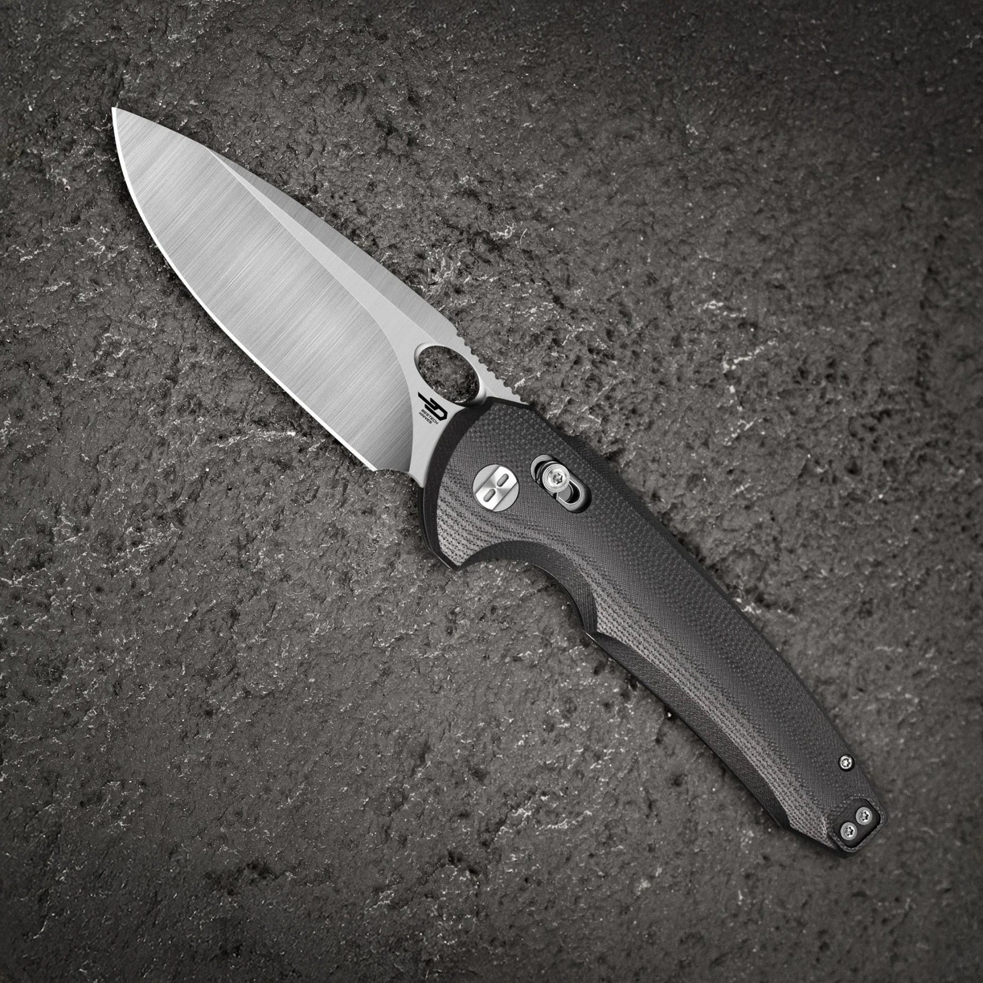 Folding knife with a brushed steel blade and black textured handle on a dark textured surface.
