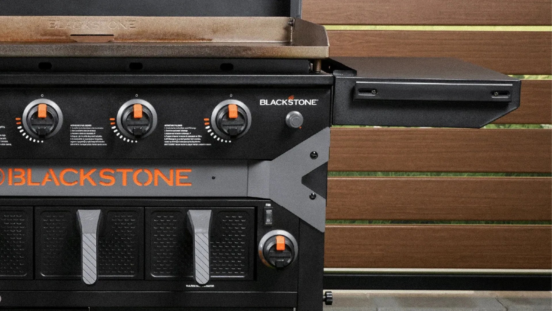Blackstone outdoor griddle with four orange and black control knobs and a side shelf attached.