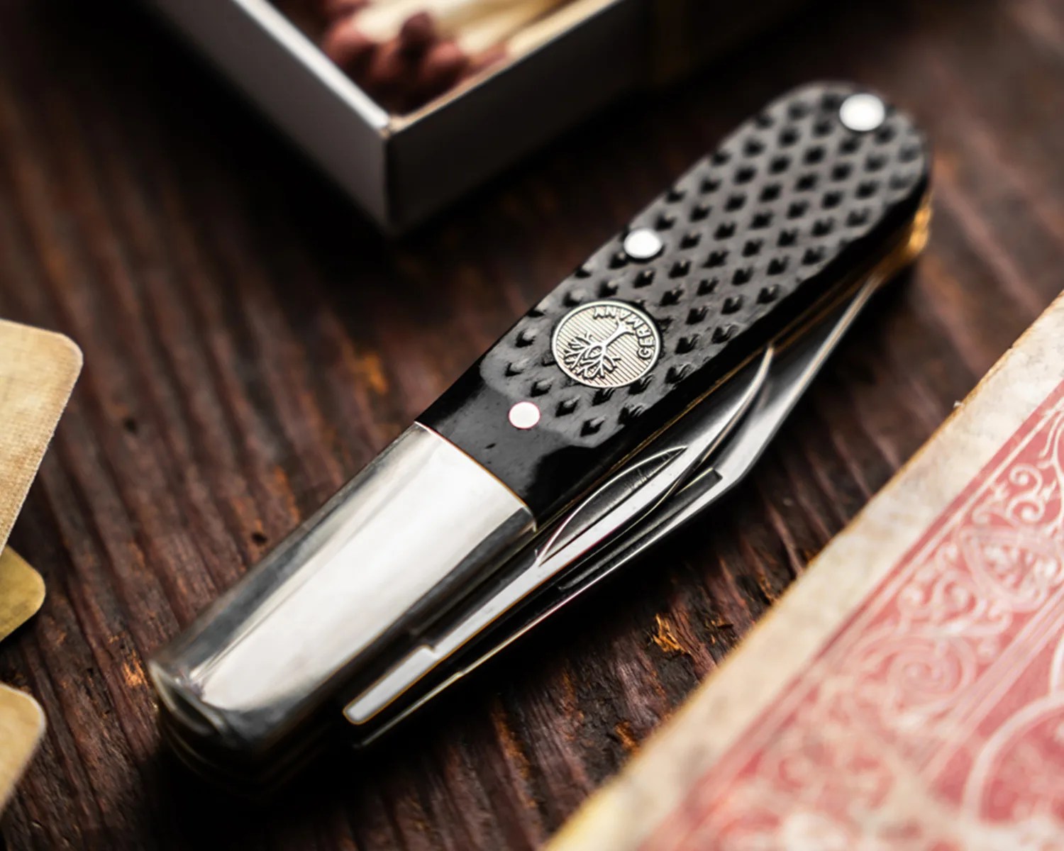 Black textured pocket knife with silver bolsters and a circular emblem on a wooden surface.