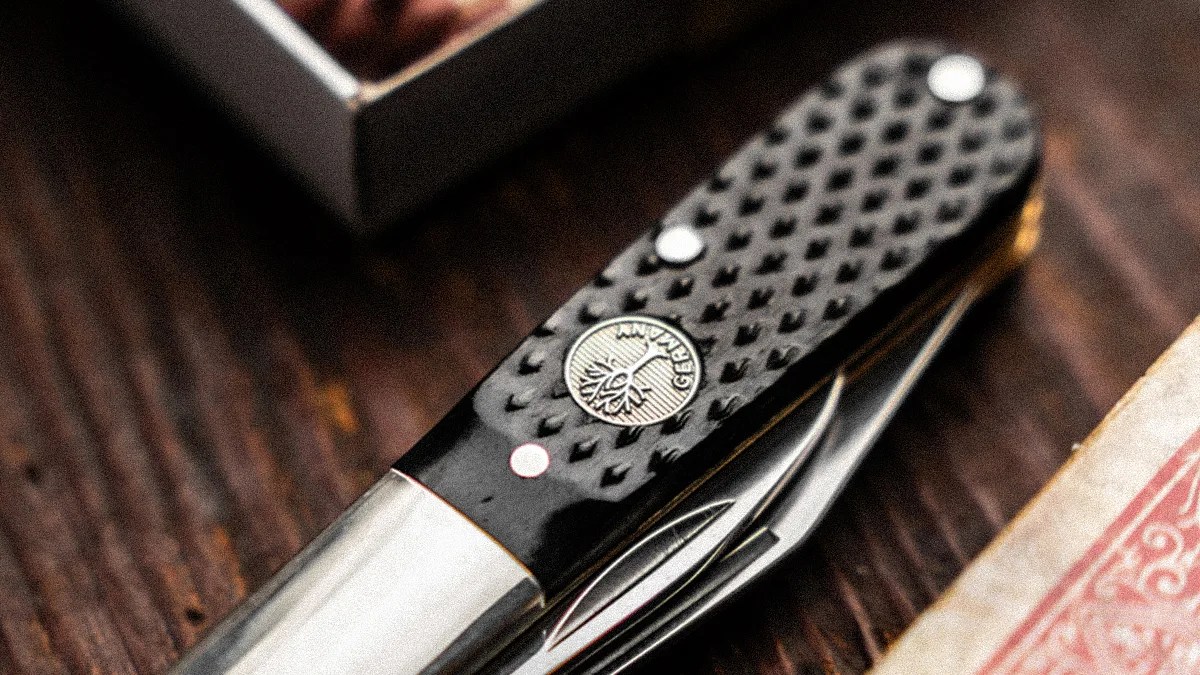 Black textured folding pocket knife with a silver emblem and partially visible blades on a wooden surface.