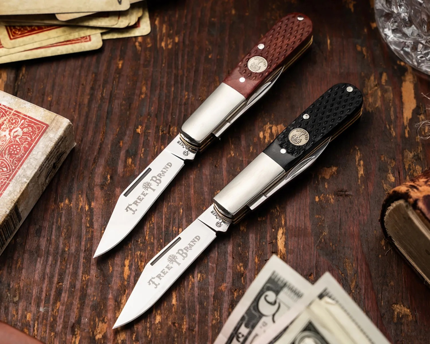 Two folding pocket knives with "Tree Brand" engraved blades, one with a brown handle and one with a black handle, on a wooden surface.