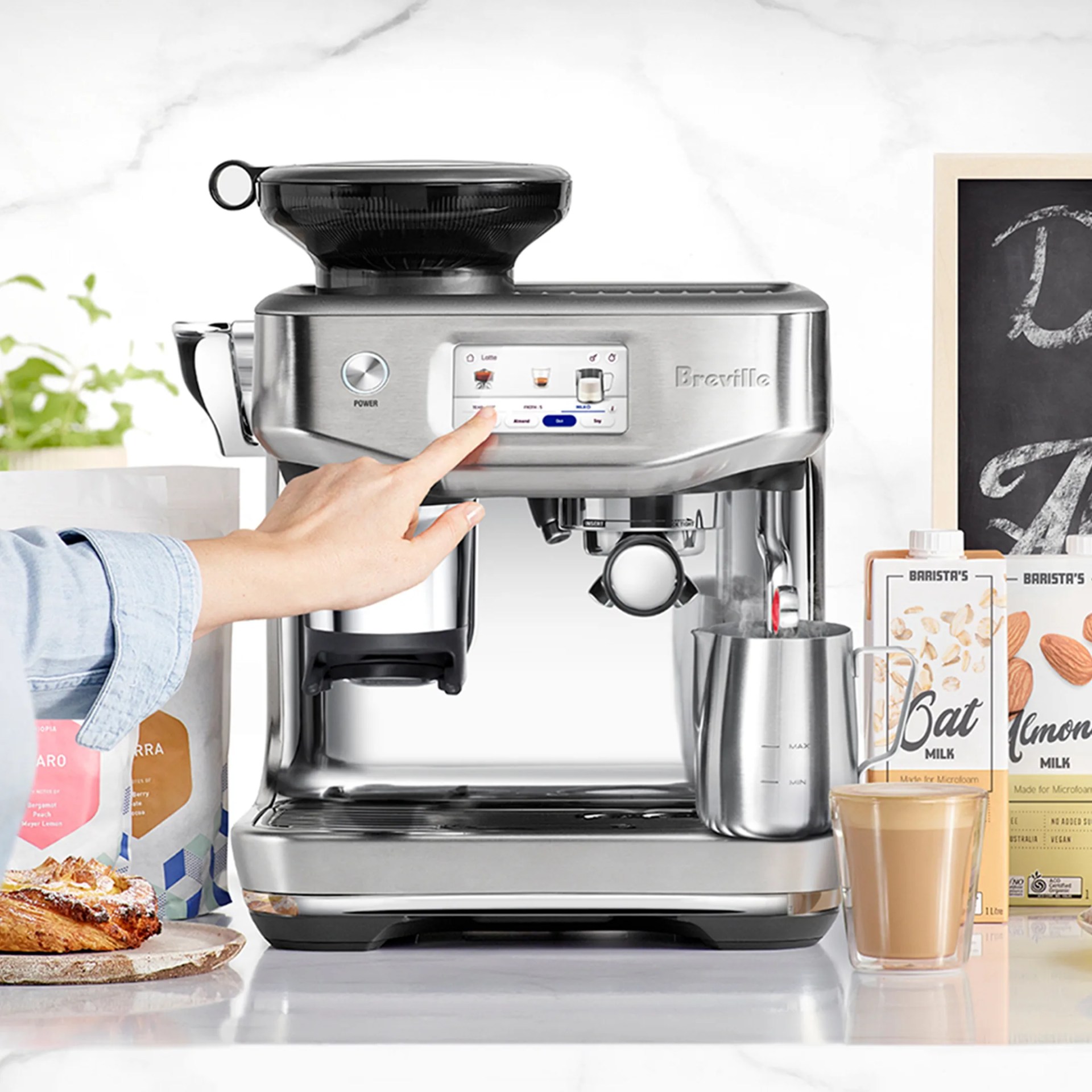 Stainless steel Breville espresso machine with touchscreen, milk frother steaming milk in a metal jug.