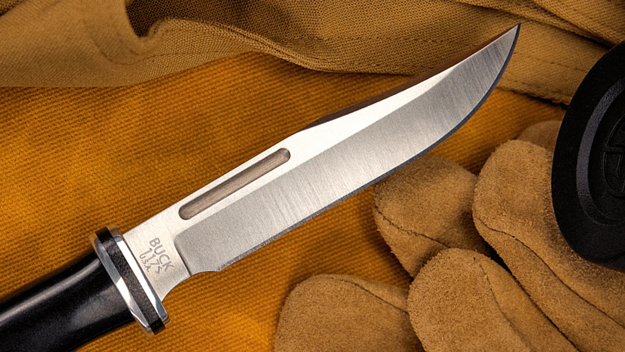 Buck 119 USA fixed blade knife with black handle resting on brown fabric and gloves.
