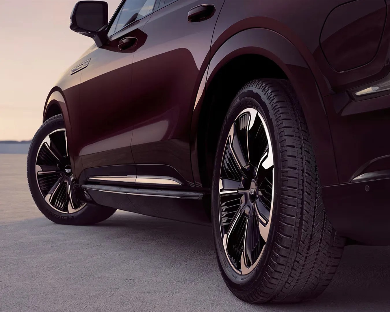 Close-up of a dark maroon SUV's side showing black and silver alloy wheels on a flat surface.