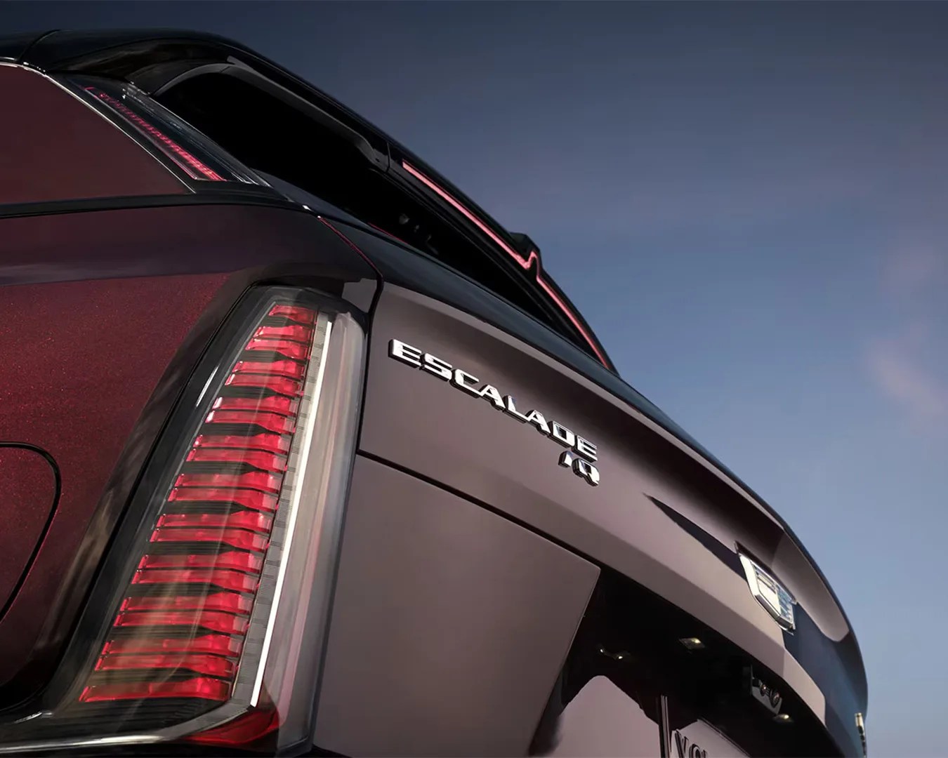 Rear close-up of a dark red Cadillac Escalade IQ showing vertical taillight and badge under a clear sky.