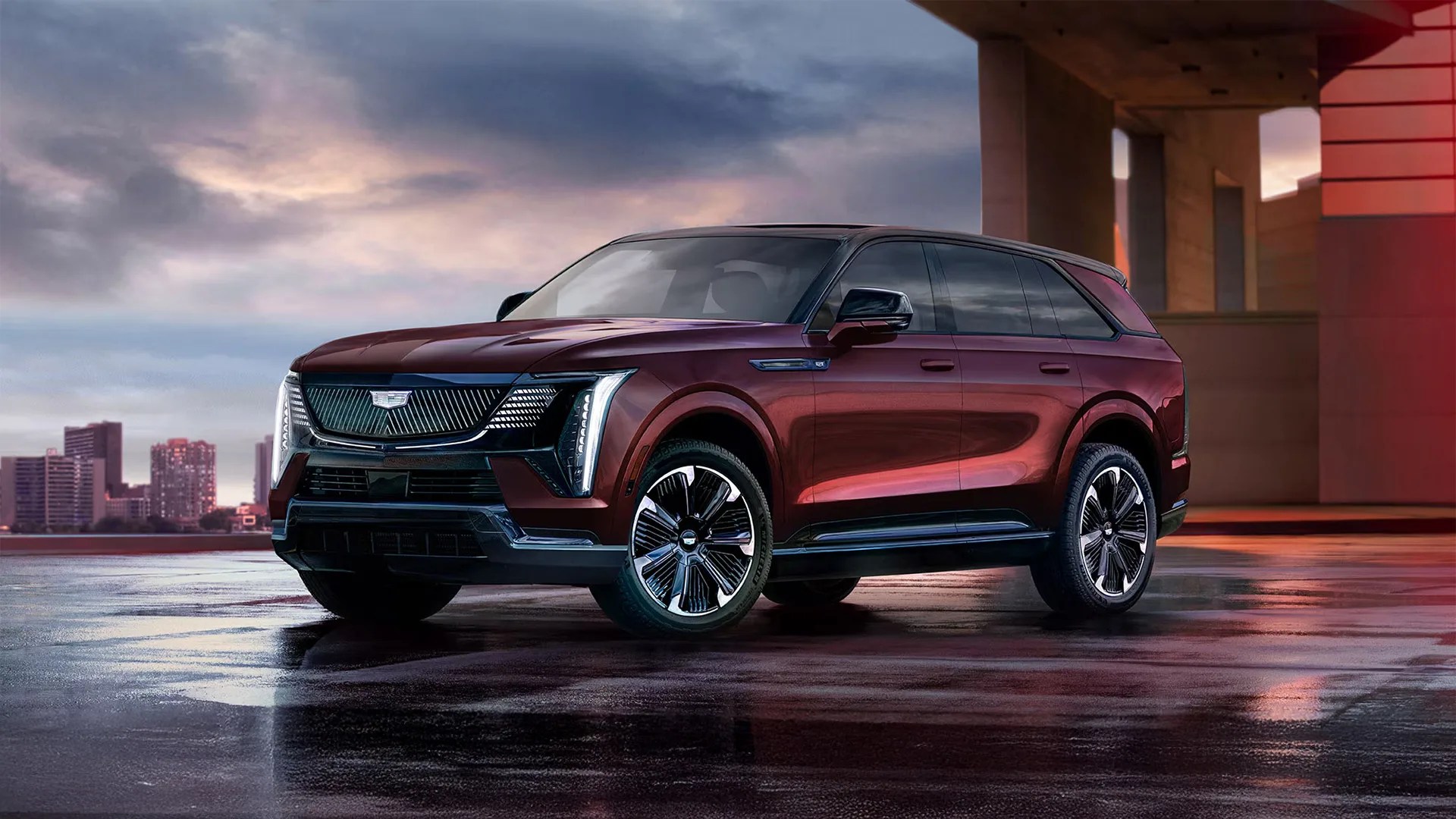 Maroon Cadillac SUV with black roof and chrome-accented wheels parked on wet pavement at dusk.