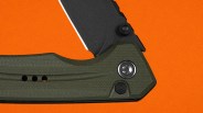 Close-up of a folding knife with a black blade and textured olive green handle on an orange background.