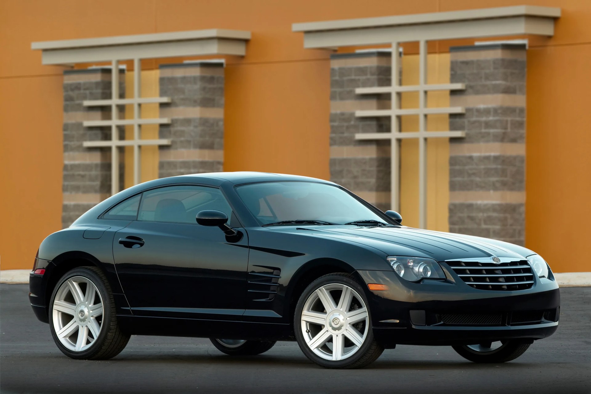 Black two-door sports coupe with silver alloy wheels parked in front of an orange and stone building.